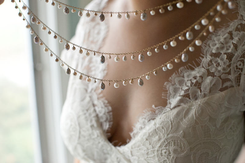 Bride puts on a unique pearl necklace for her wedding ceremony at the Morris Arboretum in Philadelphia, PA.