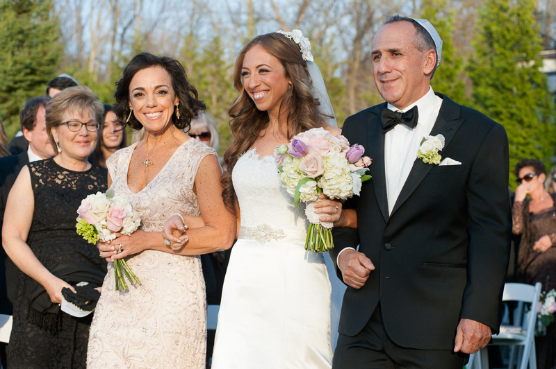 Bride walks down the aisle with both parents at her rustic wedding ceremony at the Lake House Inn.