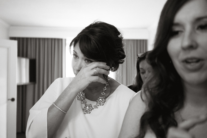 Mom cries as bride puts on her dress before her modern wedding ceremony.
