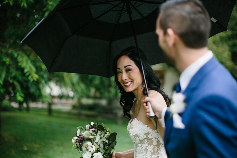 Bride and groom take cover under an umbrella during portraits.