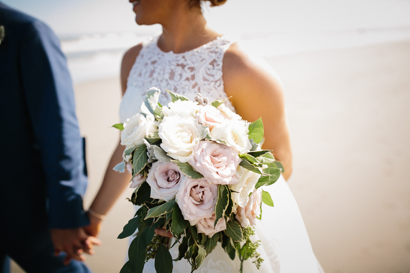 Bride holds a modern blush pink and cream bouquet at the shore.