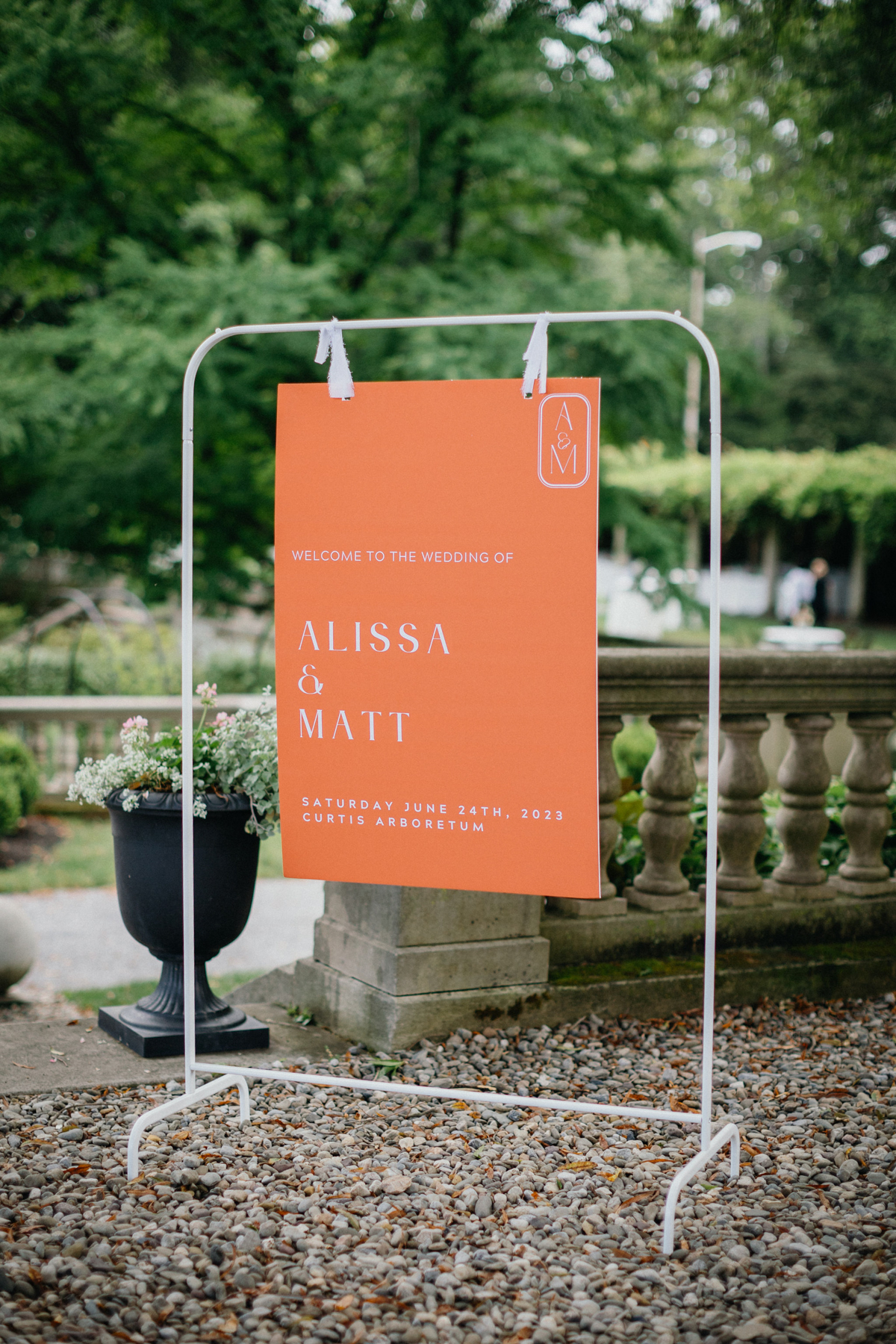 Colorful orange wedding day signage hanging on a white frame at a Curtis Arboretum wedding.