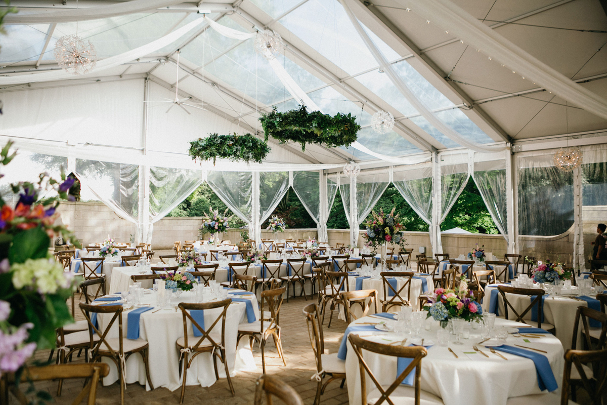 Outdoor tented Curtis Arboretum wedding reception decorated with chandeliers lined in greenery and white linens.