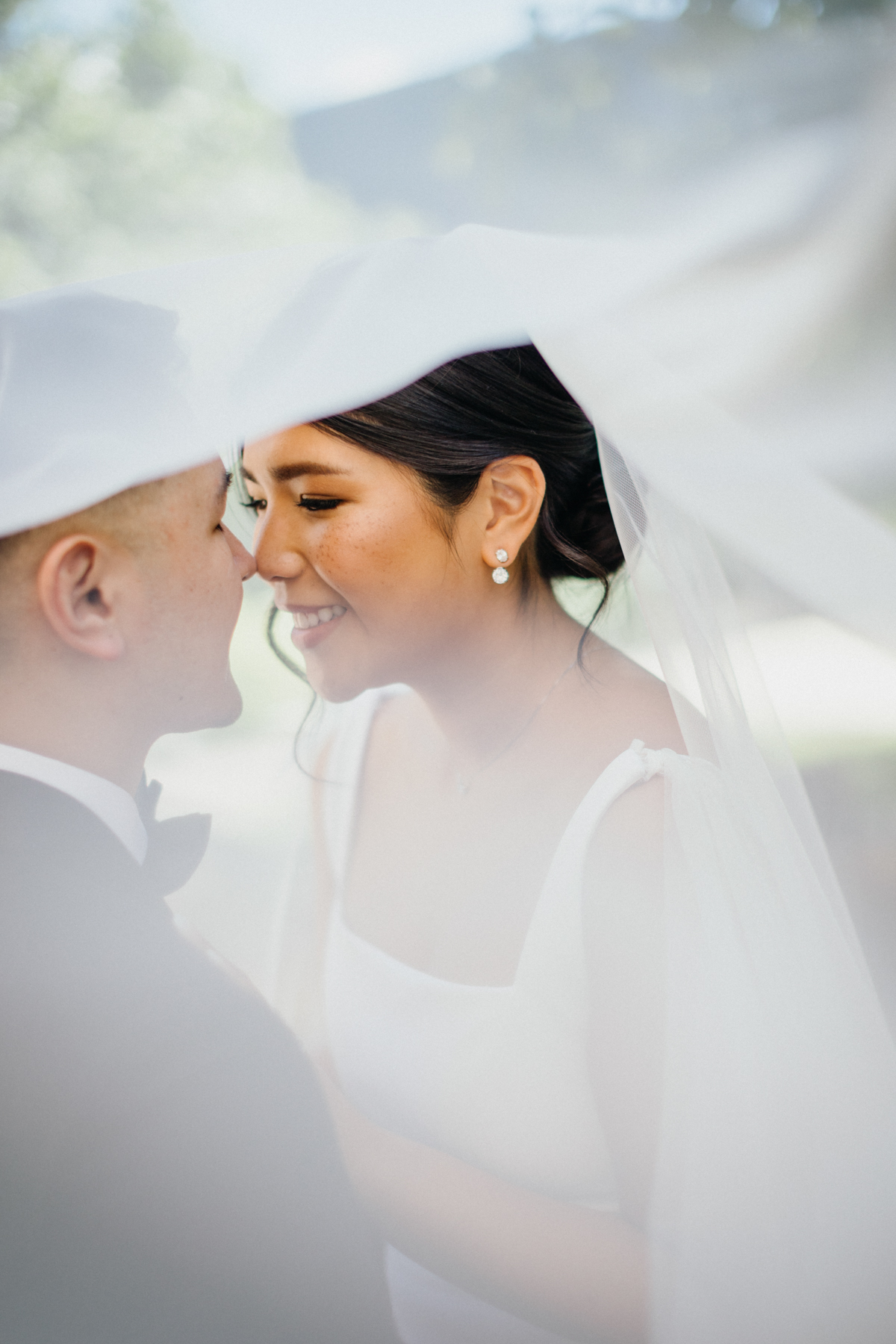 Photo of bride and groom smiling, about to kiss, underneath her veil.