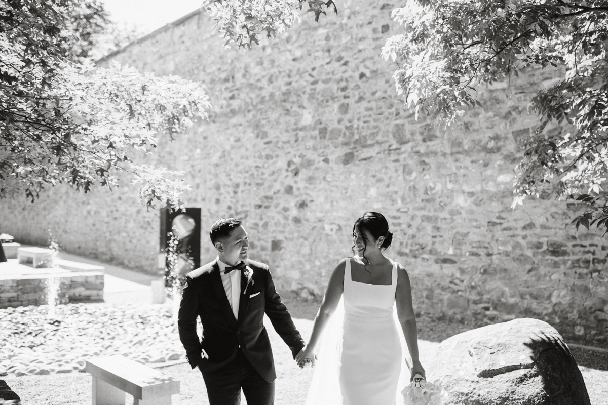 Black and white of bride and groom walking through a courtyard holding hands.