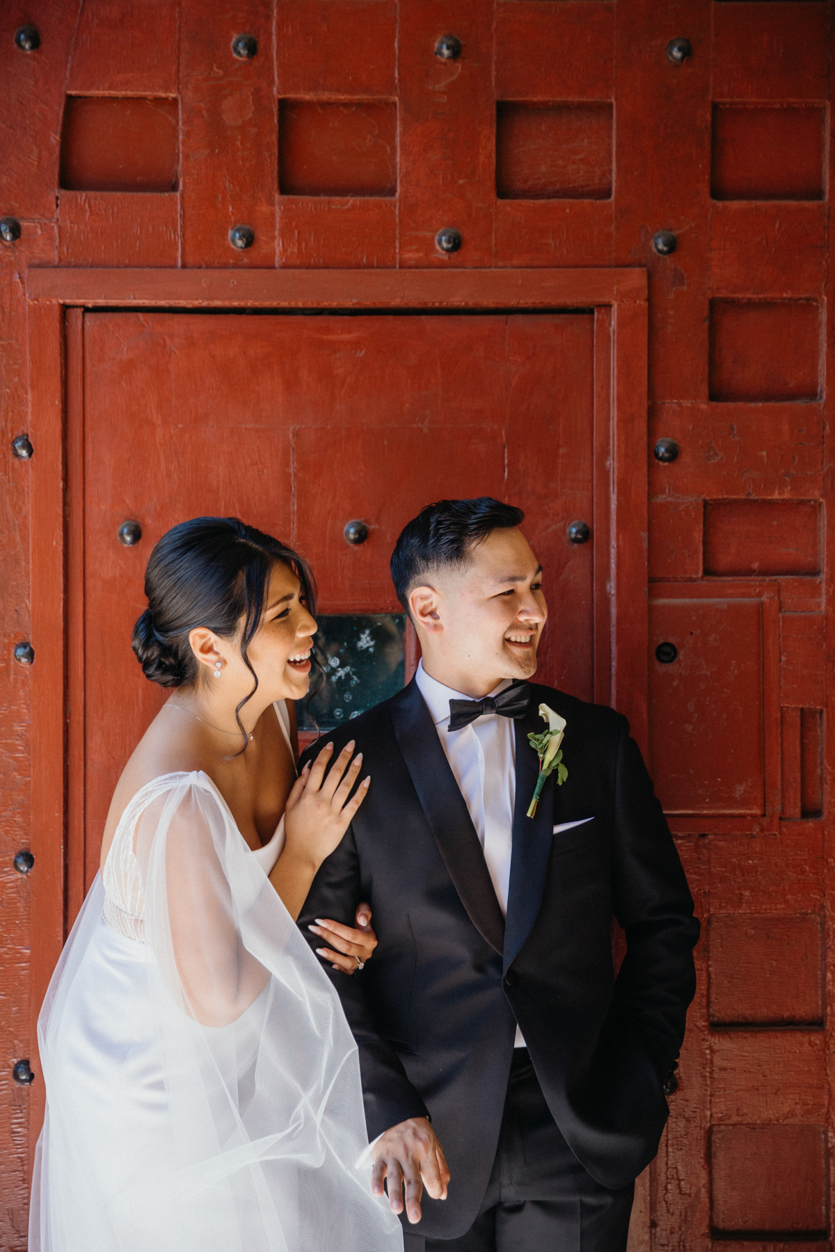 Bride and groom laugh in front of a large red door at an art museum in Pennsylvania.