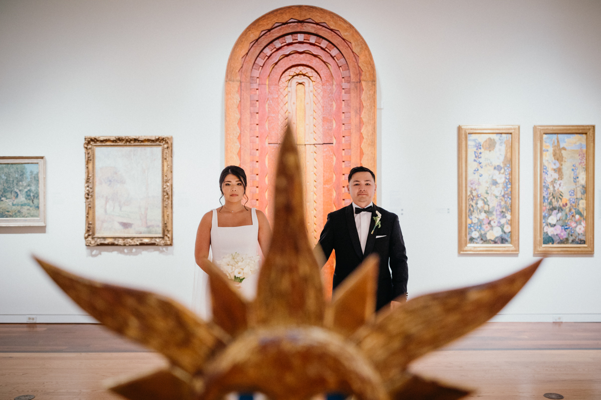 Portrait of a couple holding hands in an art gallery artfully shot from across the room.