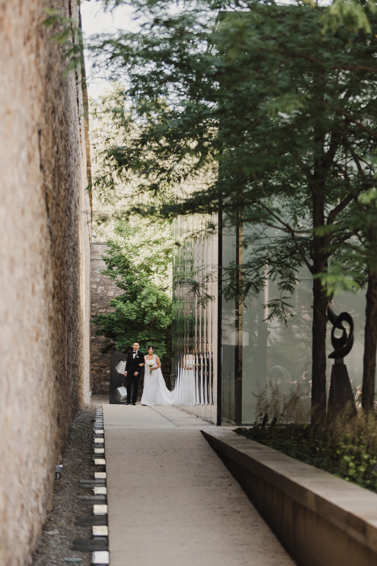 Bride walking down the outdoor aisle with a large glass reception space wall to the right.