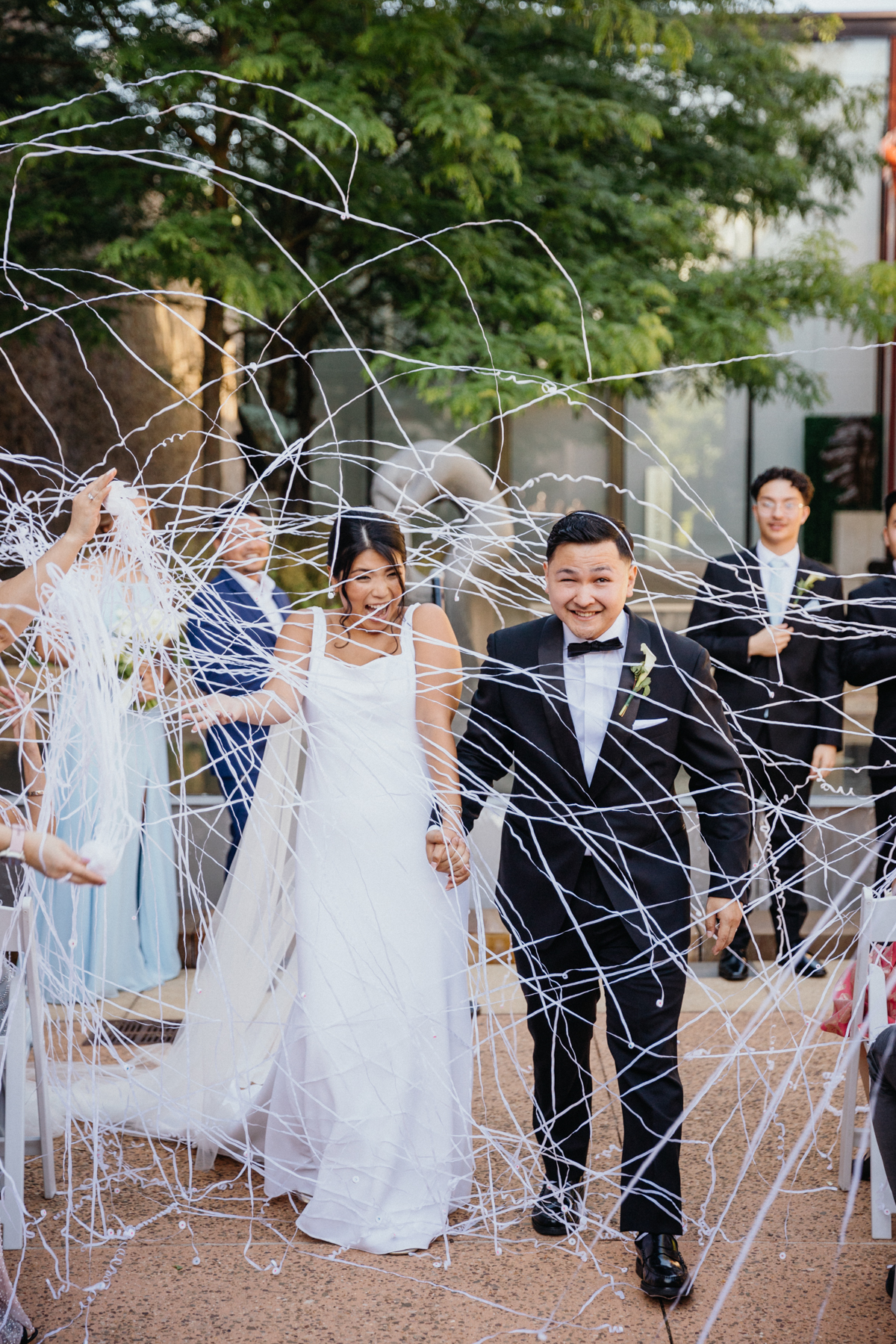 Bride and groom walking back down the aisle, laughing, as they are showered in white streamers.