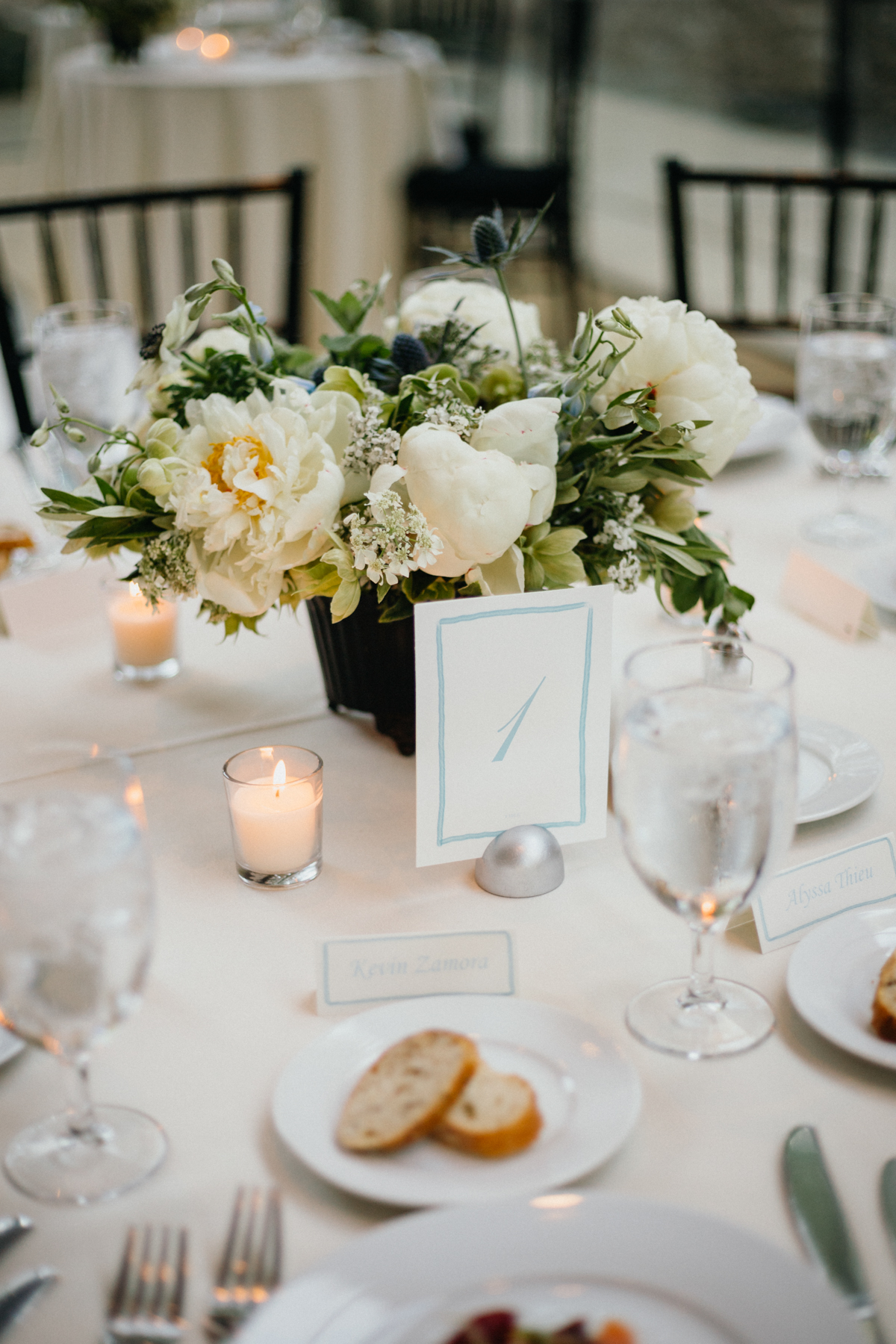 Simple and elegant light blue table numbers sitting on a table with white floral arrangements.