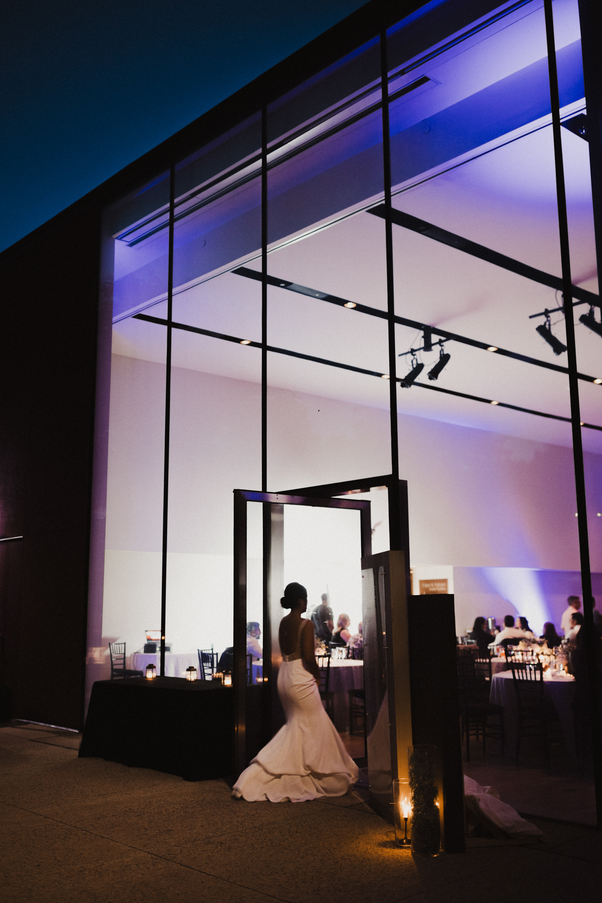 Silhouette of bride walking back into glass reception building.