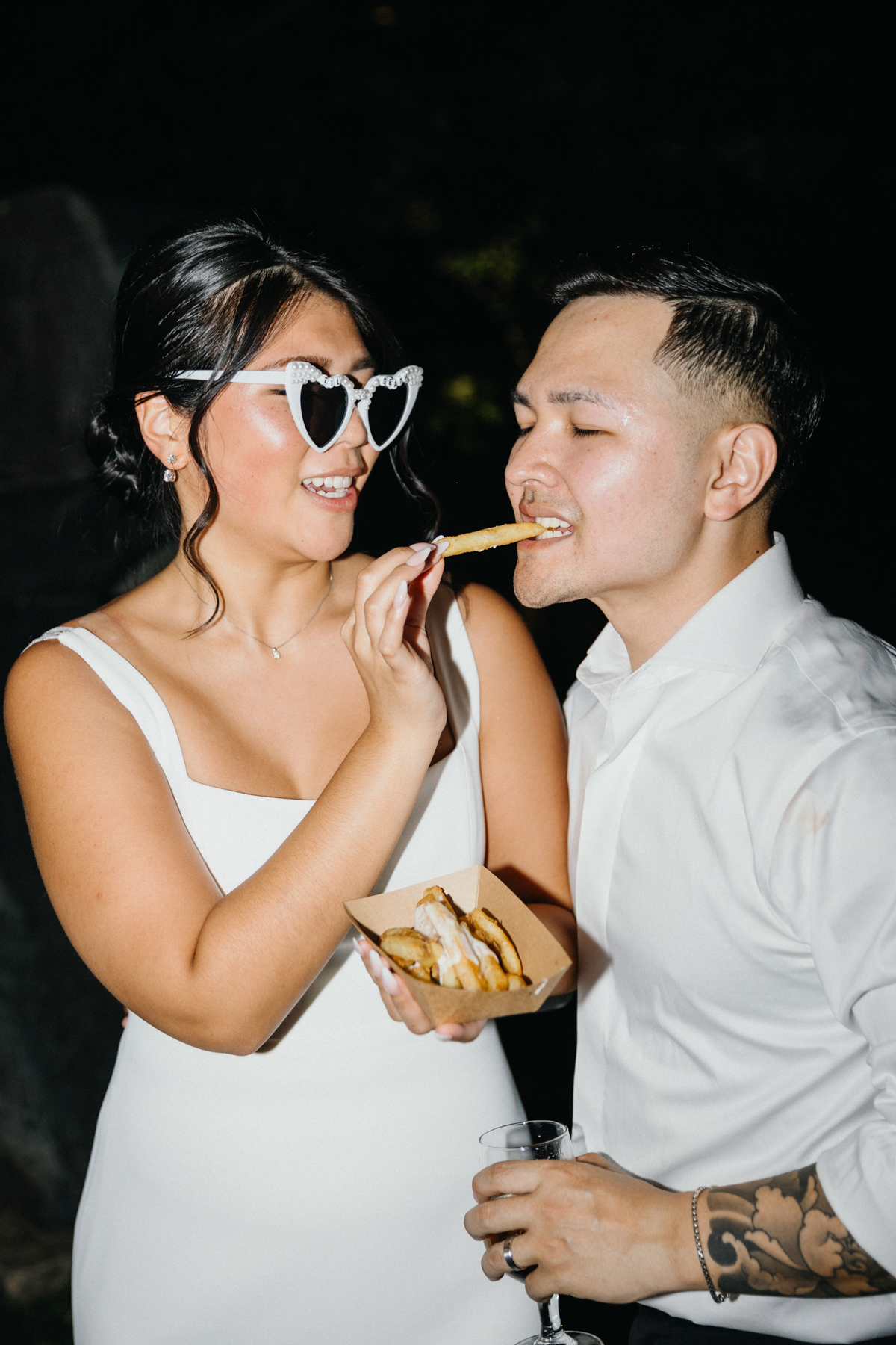 Bride feeding groom late night french fries at their wedding reception.