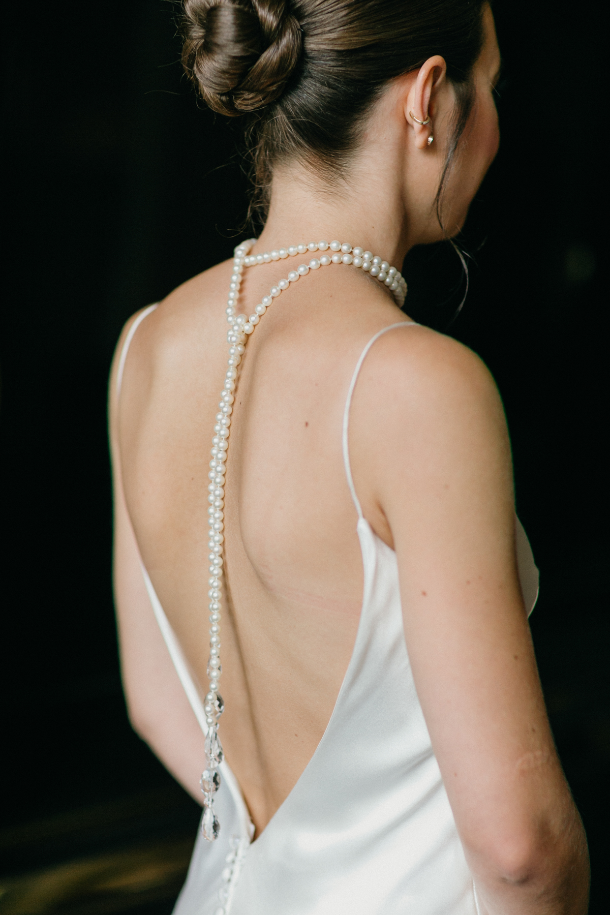 Photo of a bride wearing a pearl back necklace and a white backless slip dress.