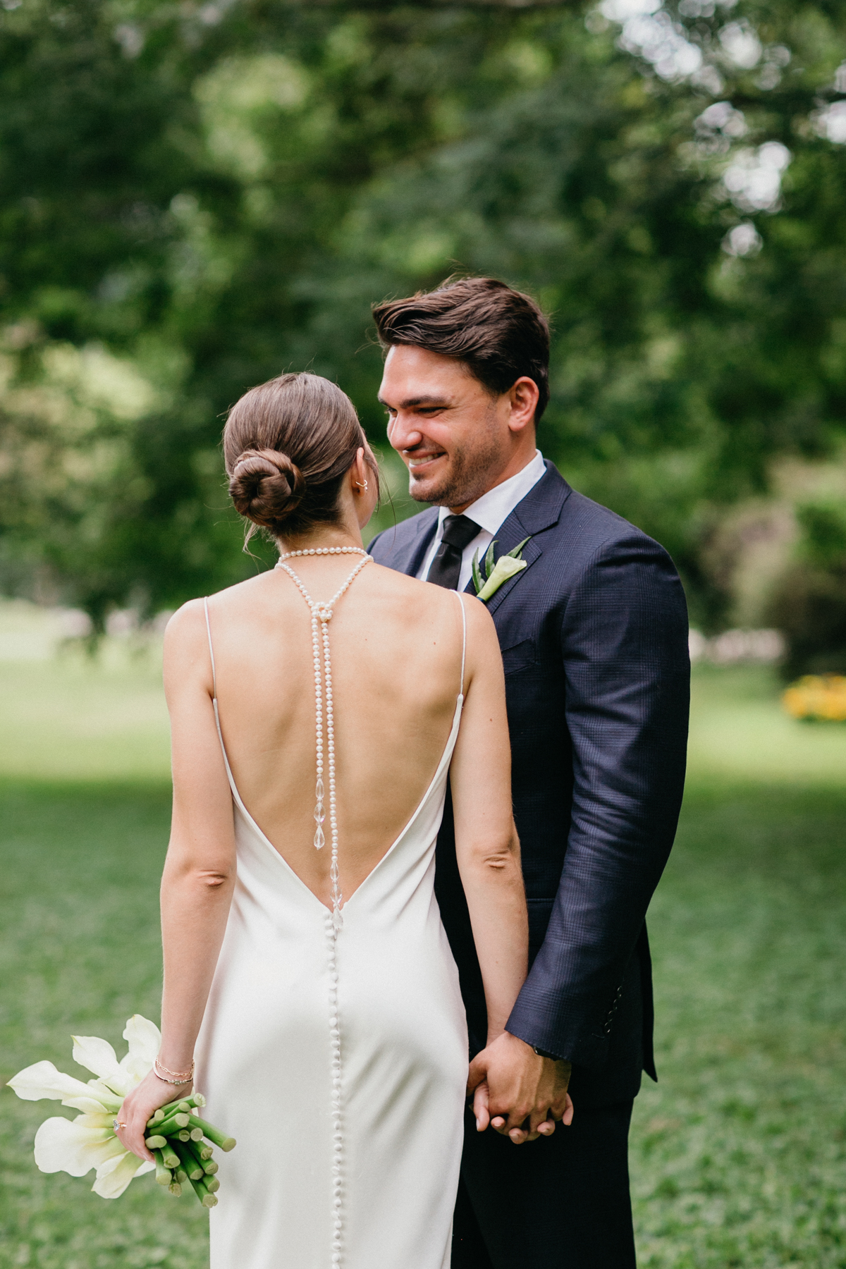 Bride and groom smile at each other surrounded by trees.