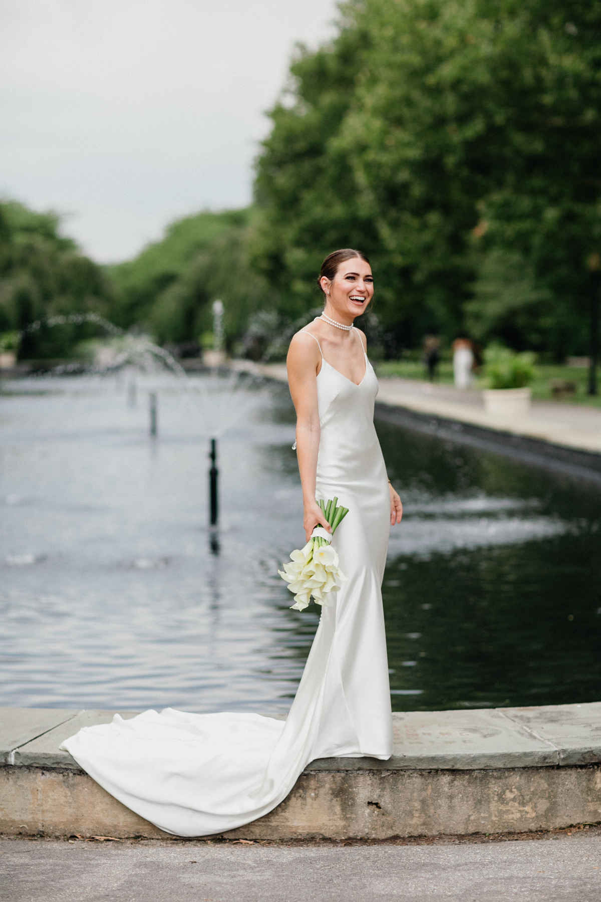 Full portrait of a bride standing on the edge of a reflection pool.