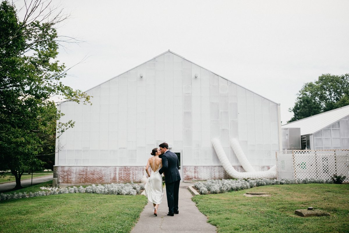 Wedding couple walking toward a white greenhouse.