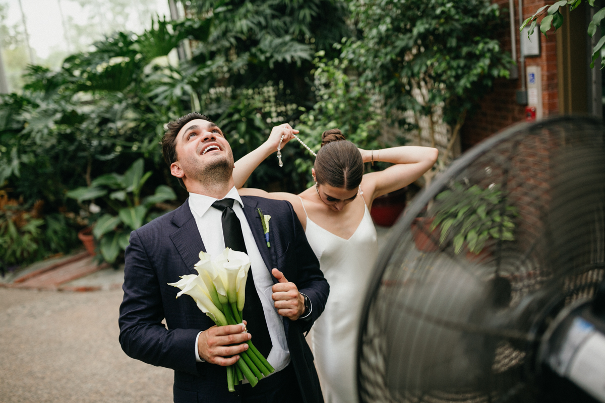 Bride and groom cooling themselves off in front of a fan.