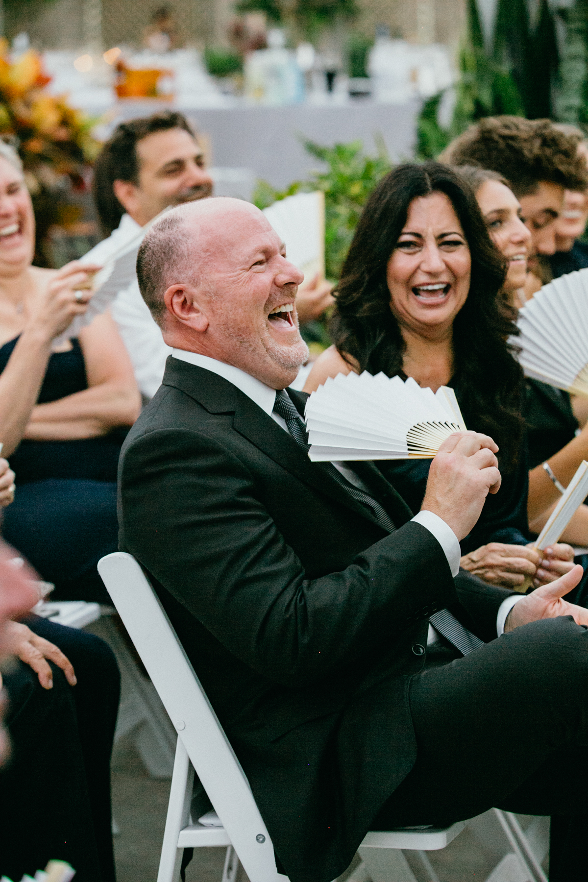 Male wedding guest laughing and fanning himself.