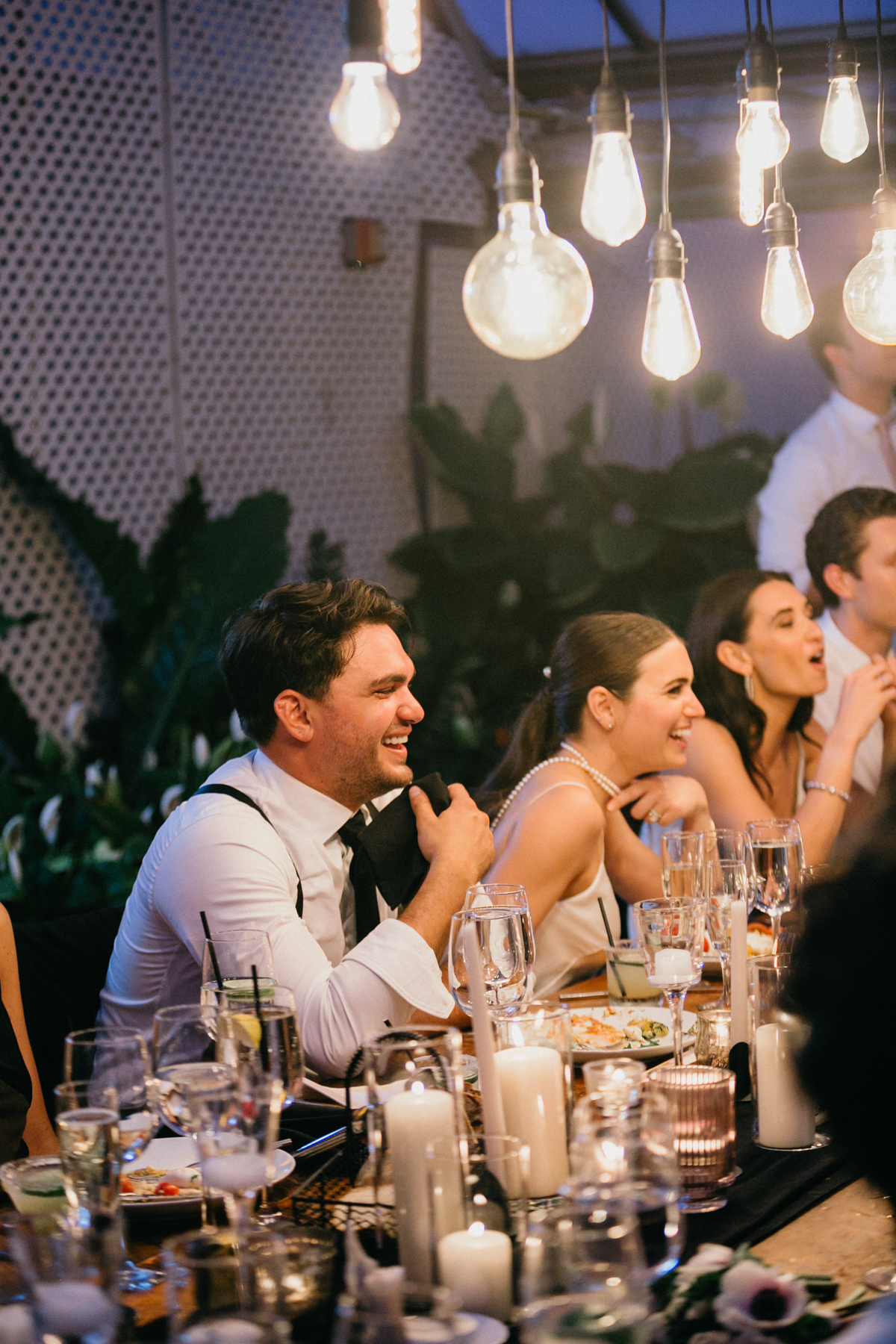 Couple and guests laugh during their wedding reception as they are seated at the table.