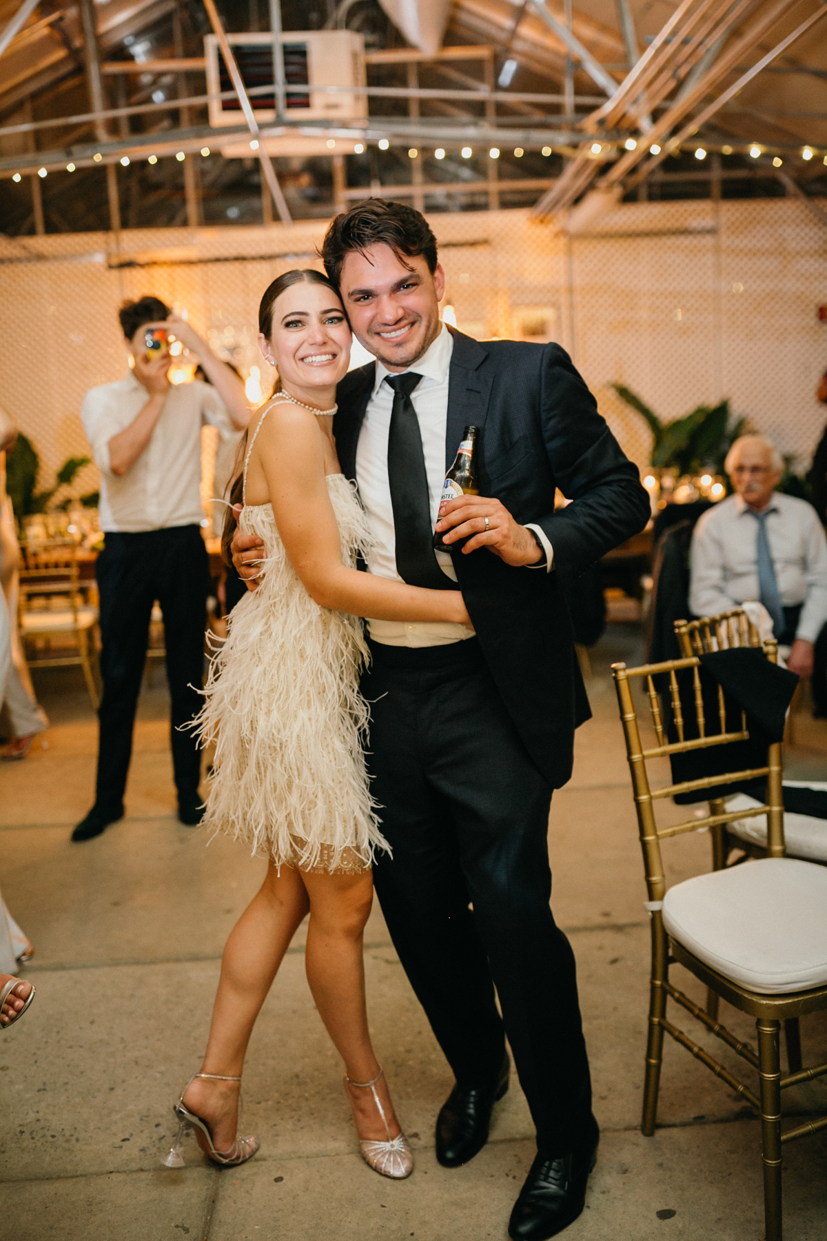 Bride and groom at their greenhouse wedding reception after her dress change. She is wearing a short fringe dress and he is in a black and white suit.