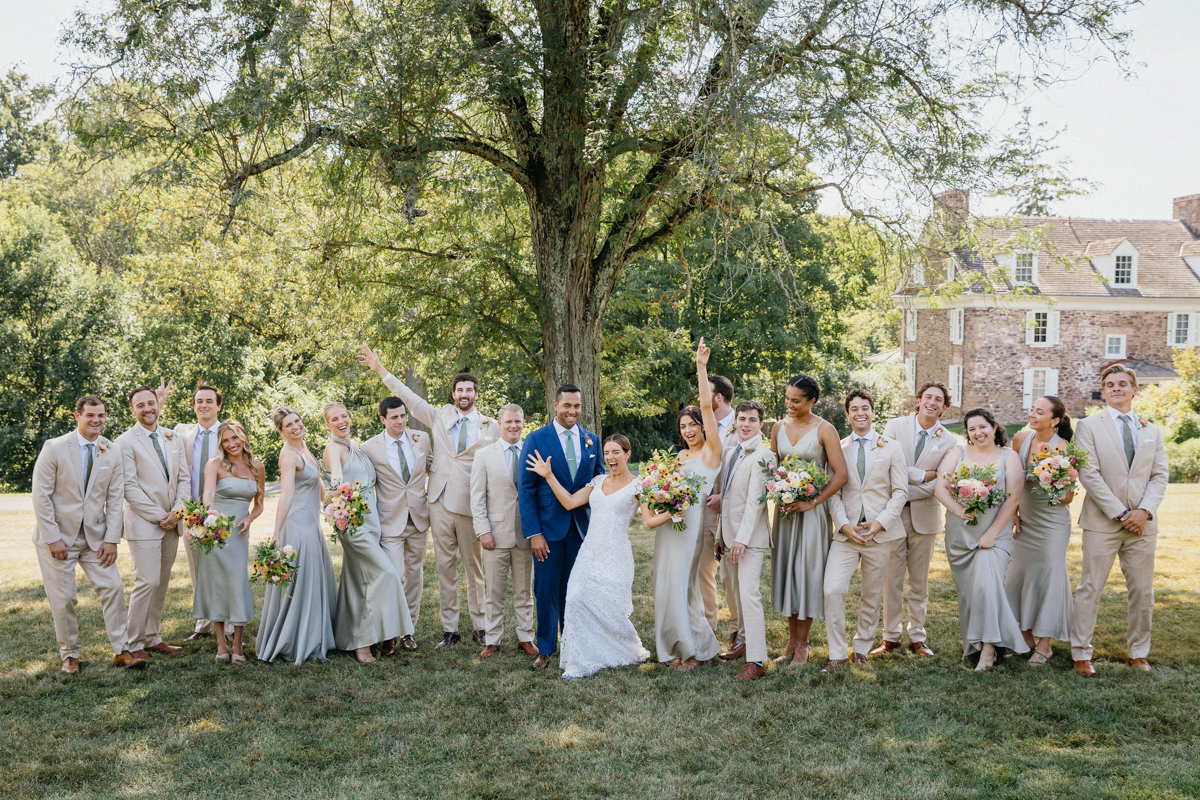 Fun photo of bride, groom, and their wedding party celebrating in the gardens of the John James Audubon Center.