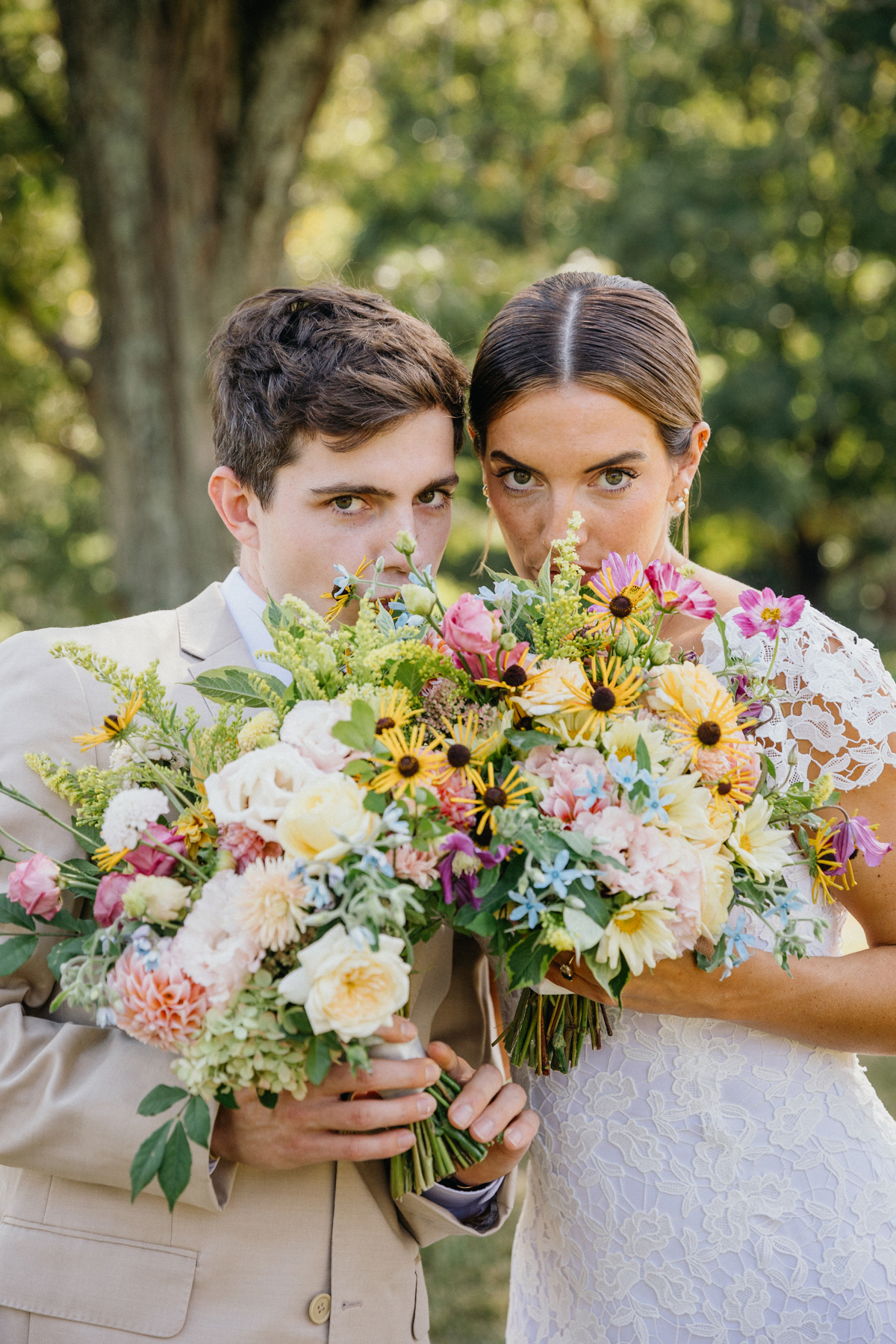 Bride and her brother holding up their colorful bouquets toward the camera.