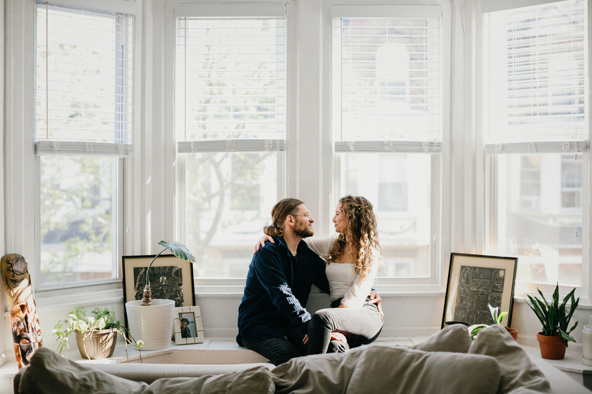 A couple cuddles on their living room couch, surrounded by books and plants in their cozy Philadelphia home.