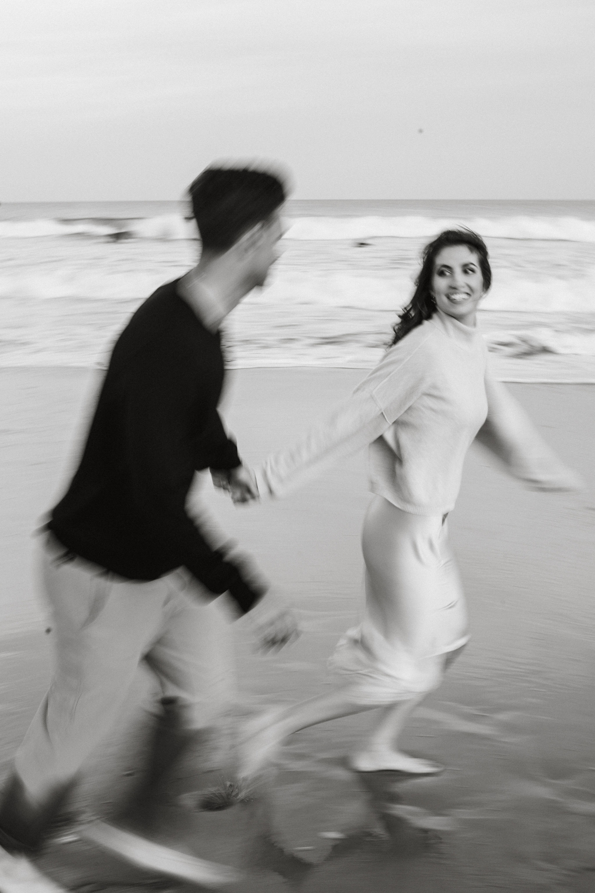 A couple walks along the beach, leaving footprints in the sand as the waves roll in.