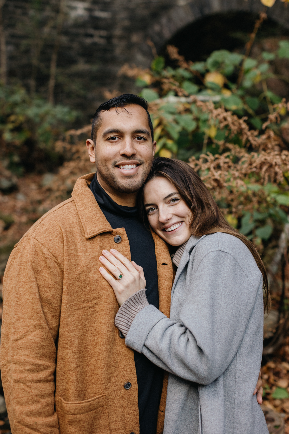 A couple stands together in a sunlit clearing surrounded by tall trees near Philadelphia.