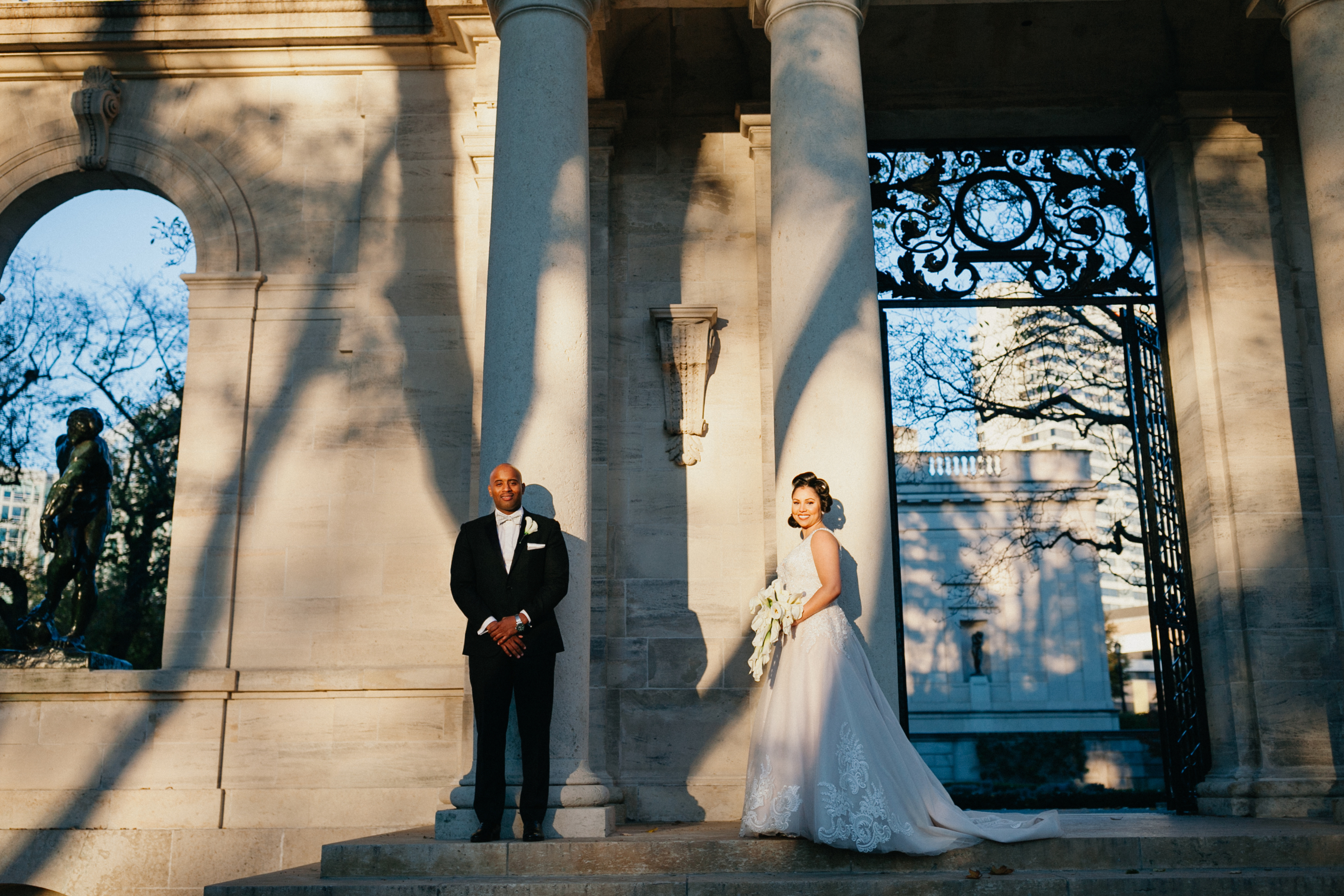 A couple stands together in an elegant garden setting, framed by classic architecture at the Rodin Museum in Philadelphia. 