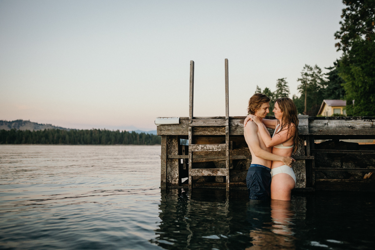 A couple swims in a clear lake, laughing as they float near the shoreline.