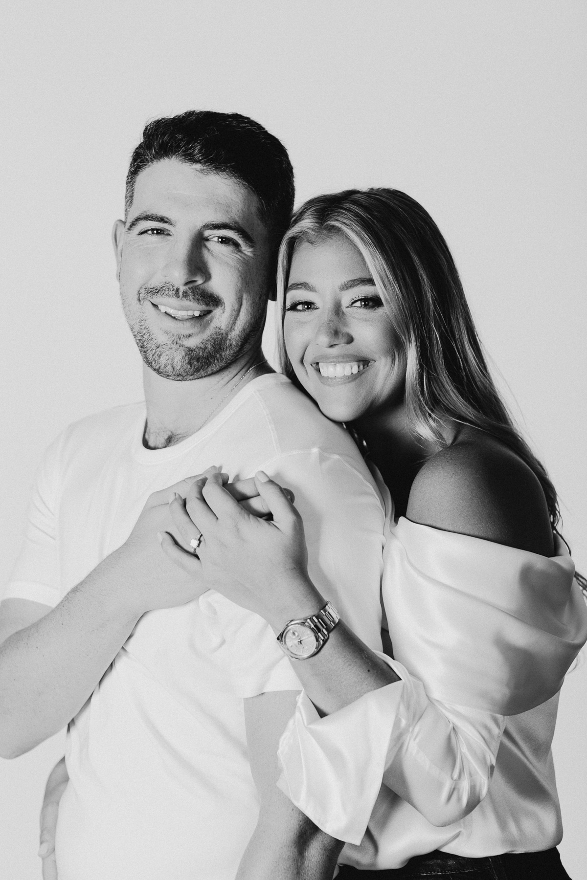 A couple poses under soft studio lighting, with a minimalist backdrop enhancing their smiles.