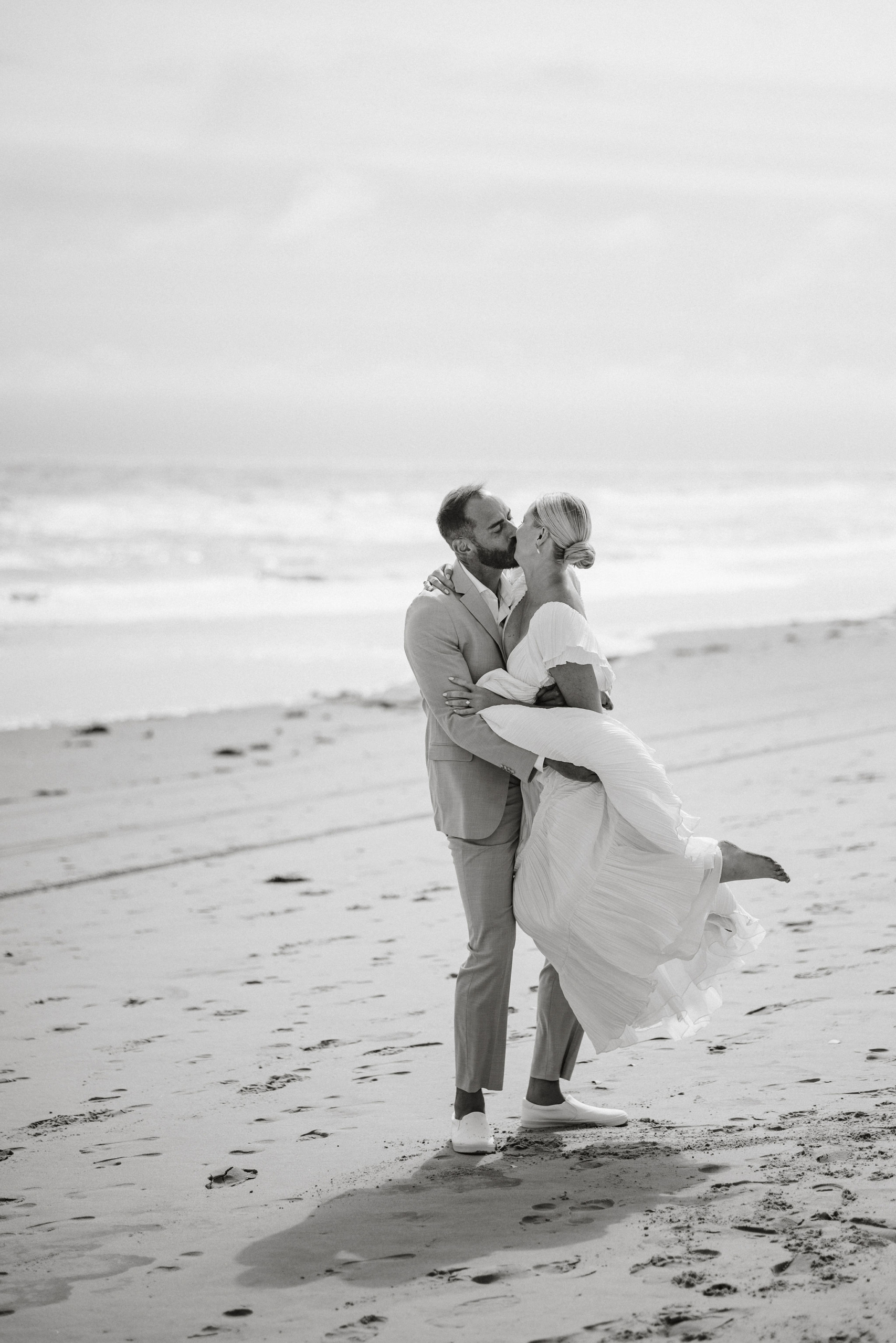 Groom lifting the bride as waves crash behind them.