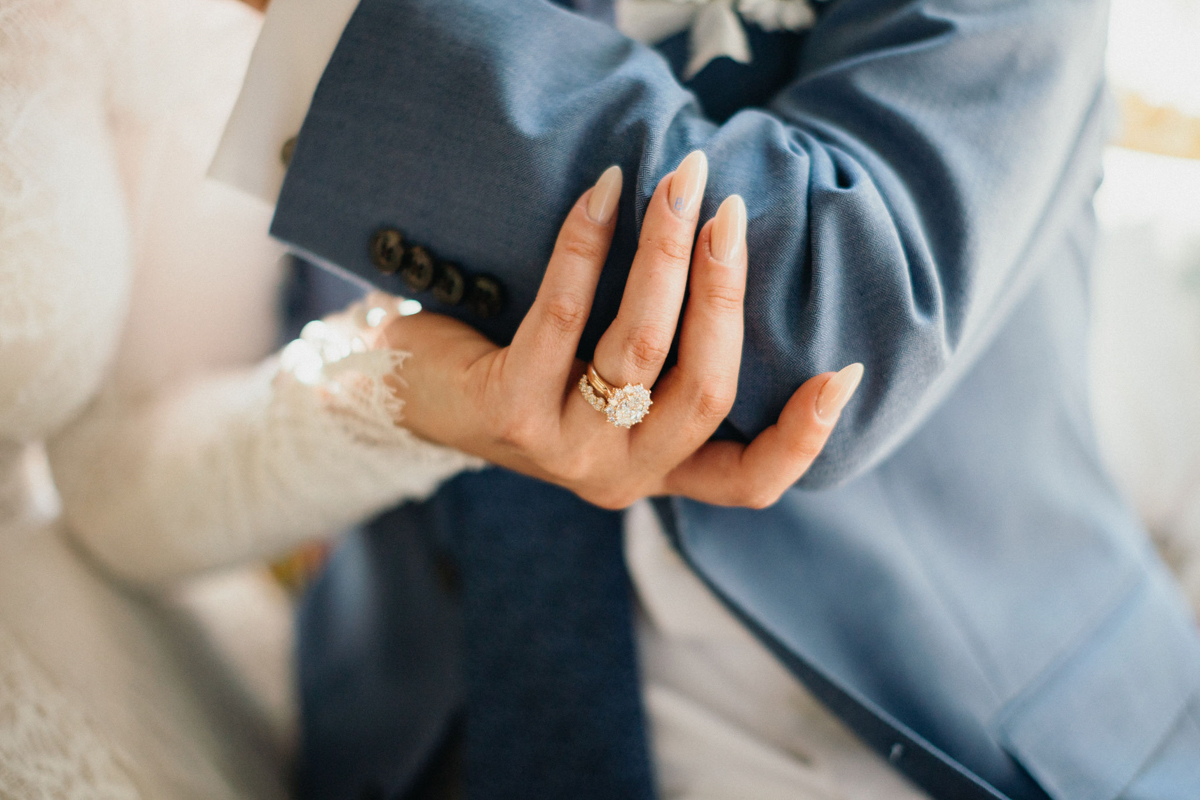 A close-up of intertwined hands, wedding rings catching the sunlight.