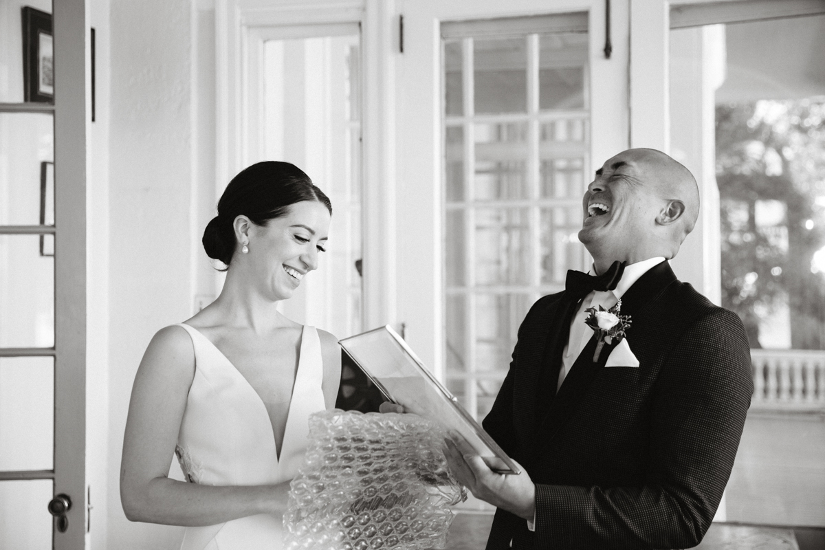Bride handing groom a wrapped gift near mansion steps – editorial wedding photography