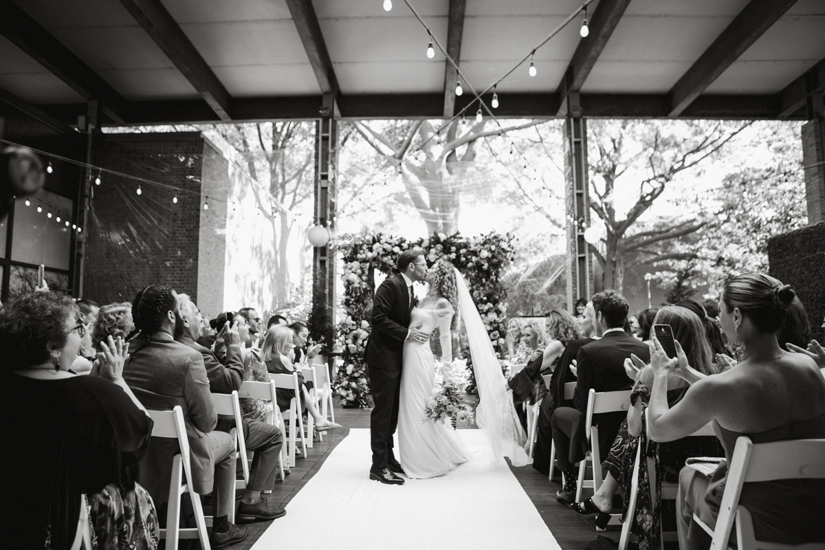 First kiss framed by natural light and florals – Zahav wedding, editorial photographer