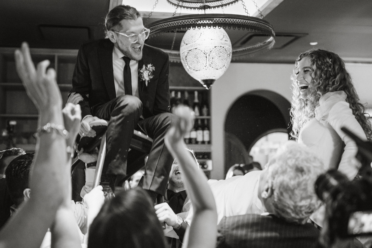 Couple lifted in chairs during the hora as guests cheer around them – Zahav wedding, Philadelphia wedding photographer