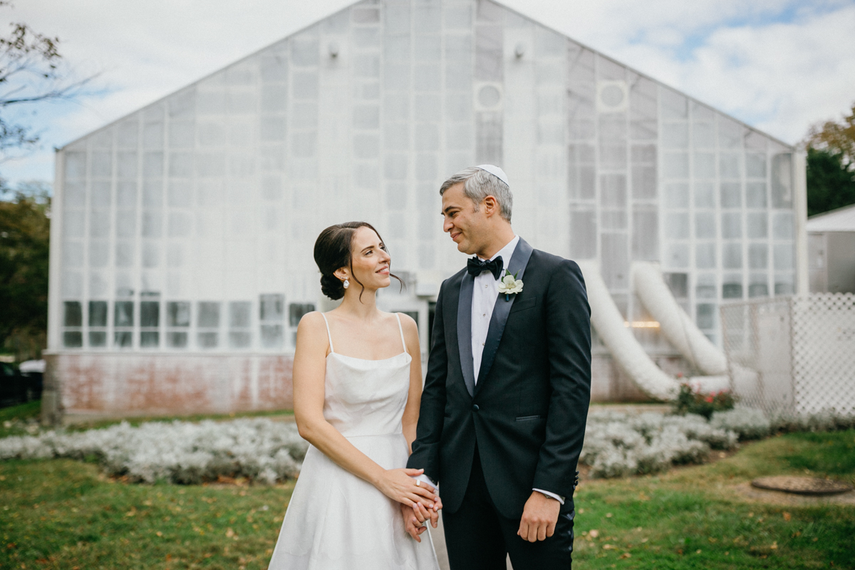 Bride and groom holding hands in front of the glass walls at the greenhouse