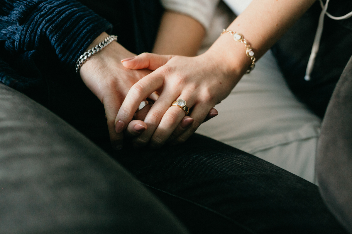 At home engagement detail photo of couple holding hands on lap
