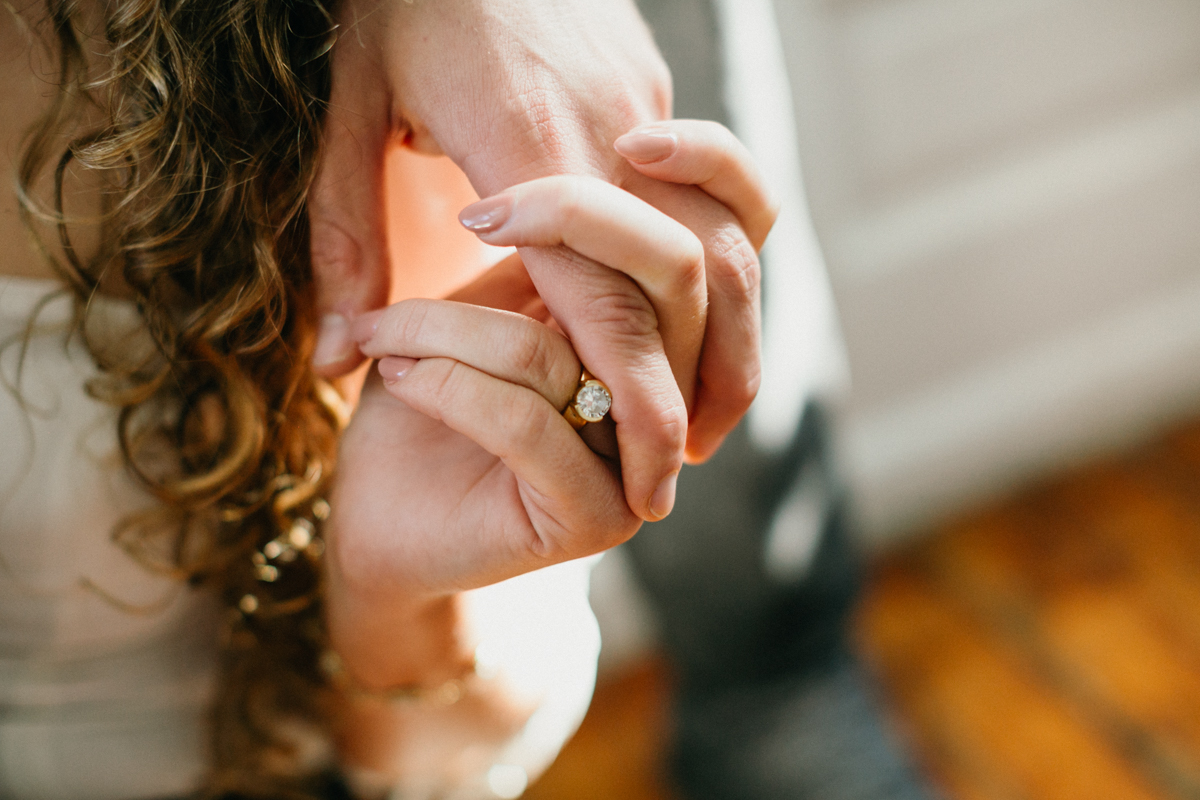 Close-up indoor engagement photo of intertwined fingers on couch