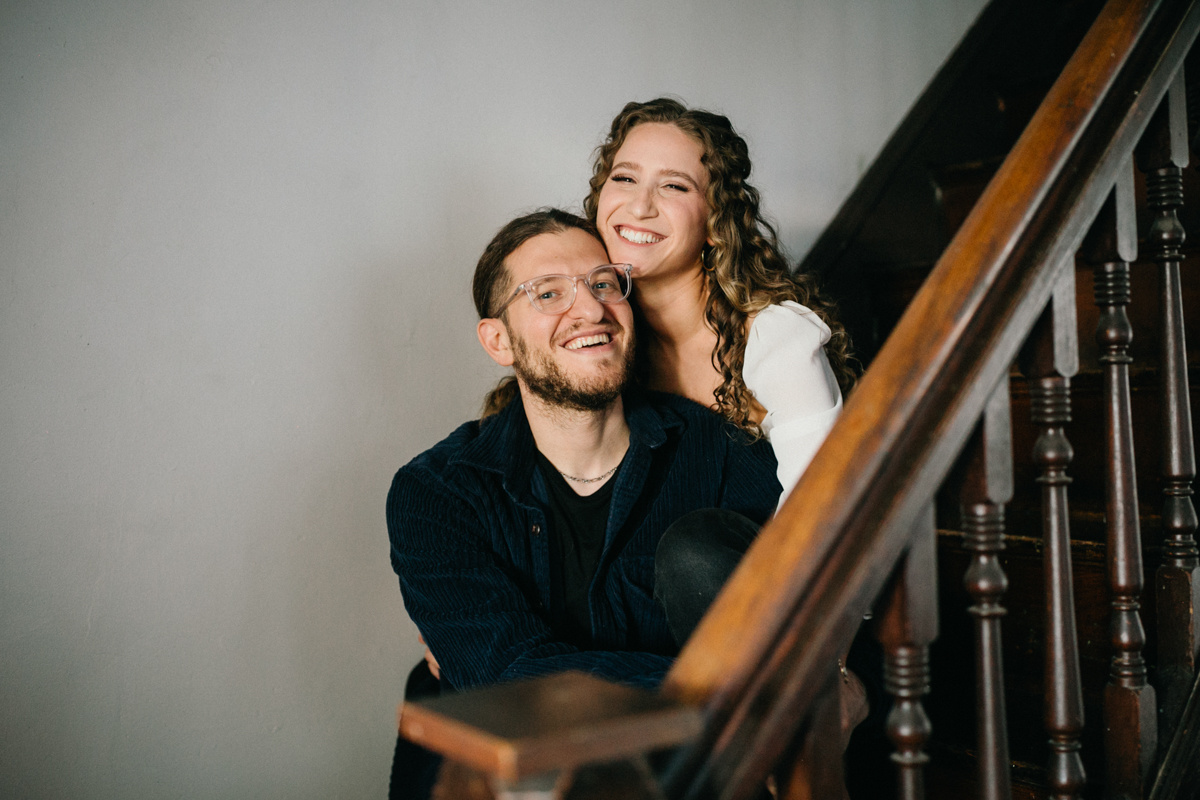 Home engagement session with couple leaning on the stair railing