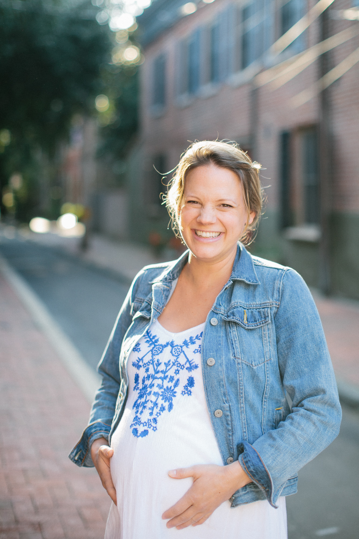 Expecting mother smiling in front of painted buildings in Philadelphia