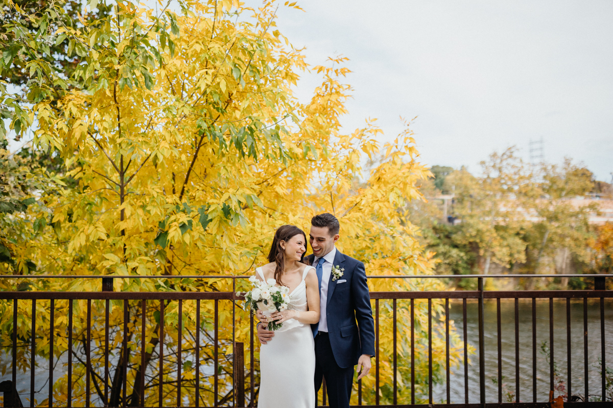 Bride and groom laughing together on waterfront bridge